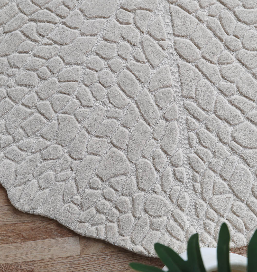 Close-up of the RAMSHA HOME Handmade Beige Color Area Rug HTW 103, featuring a raised, irregular stone-like pattern on a wooden floor; a green plant appears partially in the bottom right corner.