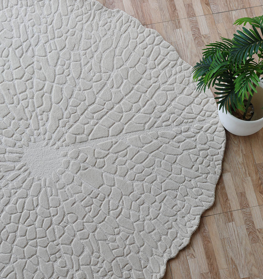 The RAMSHA HOME Handmade Beige Color Area Rug HTW 103, featuring a round, textured design with a stone-inspired pattern, lies on a wood floor with a green potted plant nearby for a stylish, neutral look.