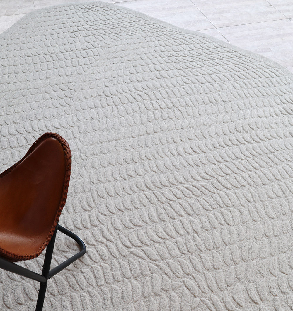 A brown leather chair with a black metal frame sits by smooth, raked sand bordered by light tiles and complemented by the RAMSHA HOME Beige Color Shape Handmade Rug HTW 104.