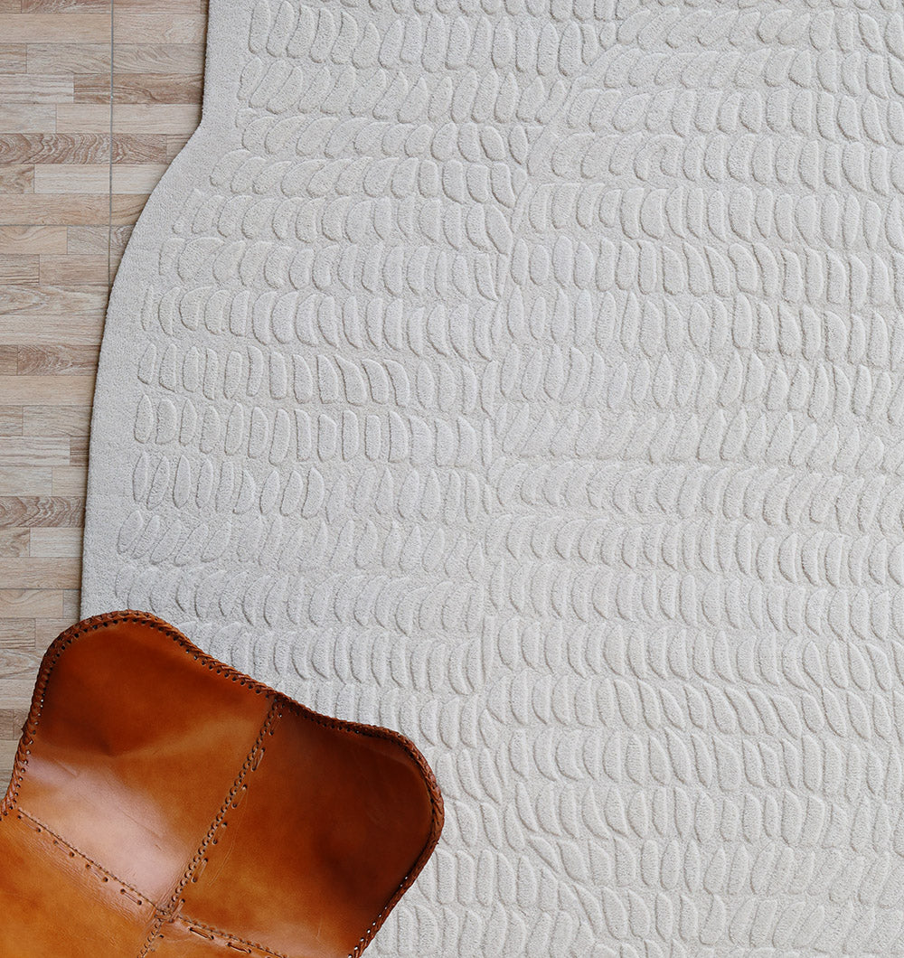 A tan leather chair sits on the Beige Color Shape Handmade Rug HTW 104 by RAMSHA HOME, which features a modern oval pattern, next to a section of wood flooring.