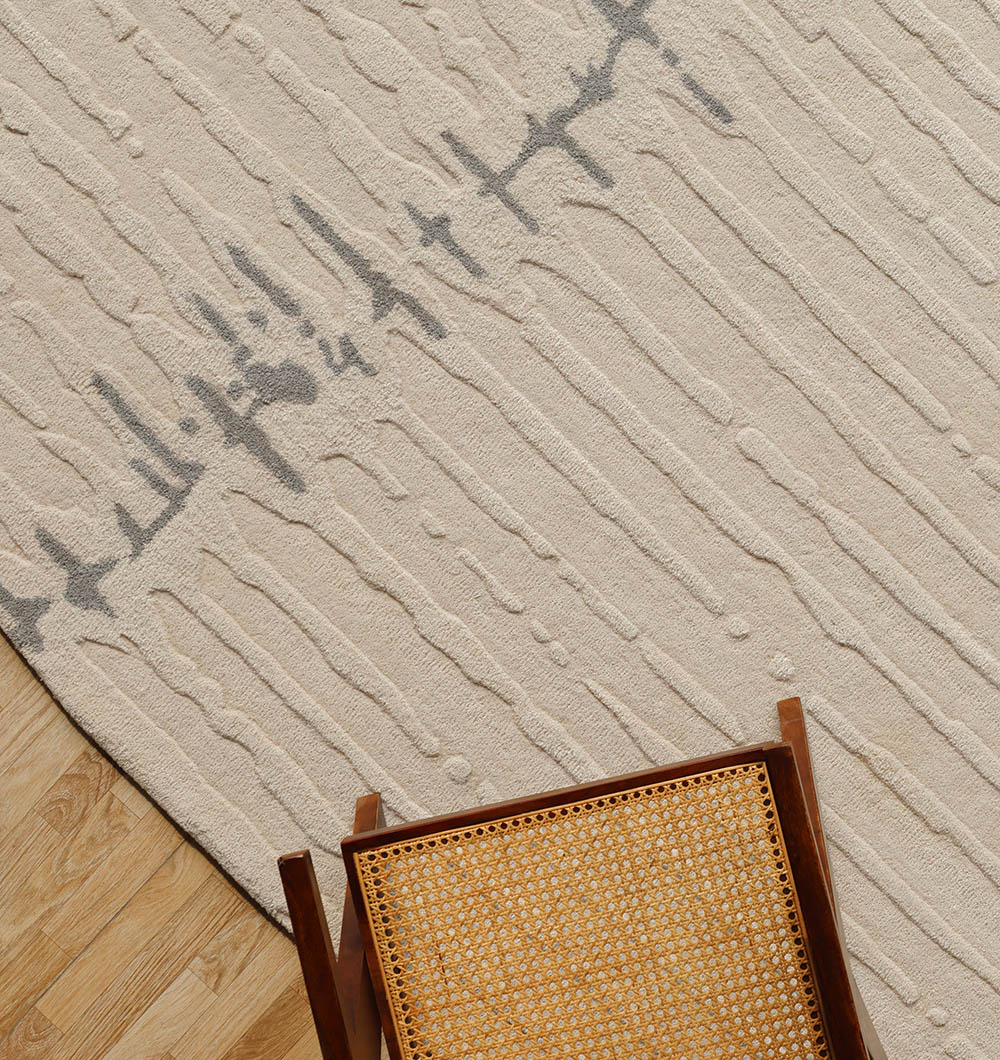 The RAMSHA HOME Irregular Shape Handmade Rug HTW 108 features a beige base with gray abstract lines and is shown beside a wooden chair with a woven cane seat, placed on a light wood floor.