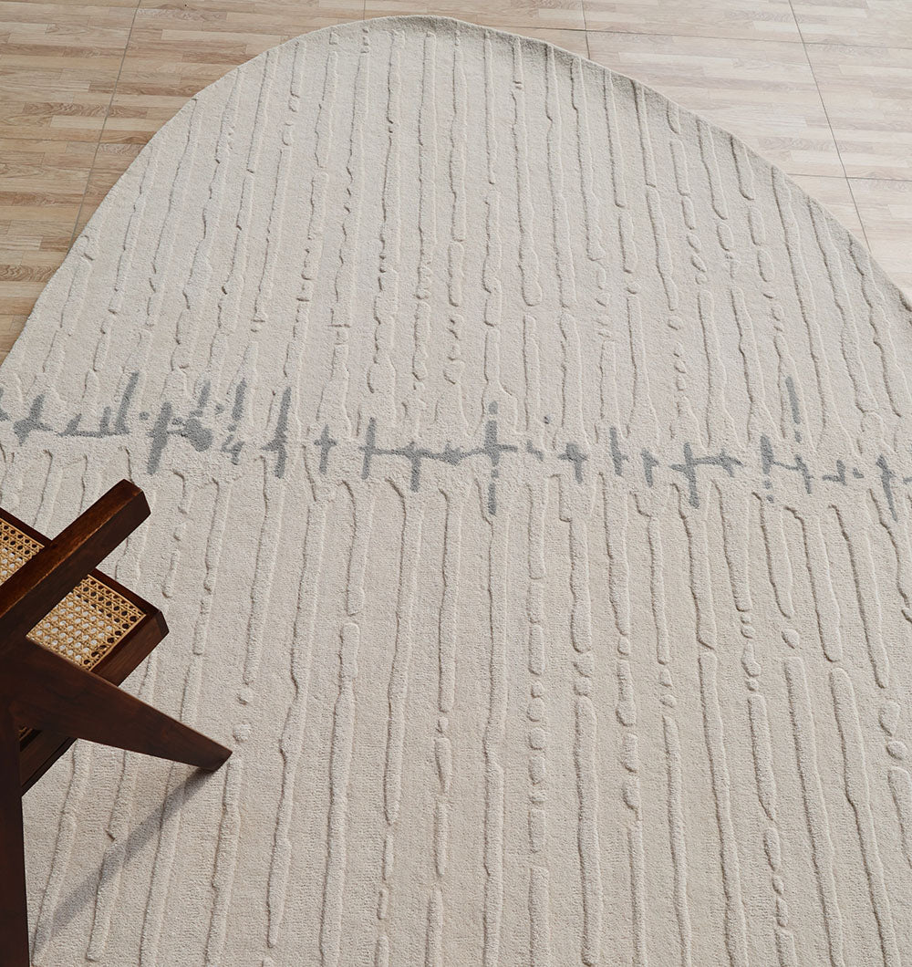 The RAMSHA HOME Irregular Shape Handmade Rug HTW 108, a beige hand-tufted wool rug with raised vertical lines and a wavy gray pattern, lies on a light wood floor, partially beneath a wooden chair with a woven cane seat.