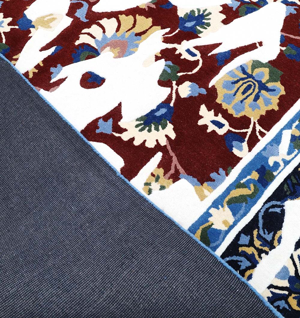 Close-up of a corner of the RAMSHA HOME Multi Color Handmade Area Rug - HTW 111 (300X400 cm), featuring vibrant red, blue, yellow, and cream floral patterns. The rug is flipped to show its plain dark blue or gray backing.