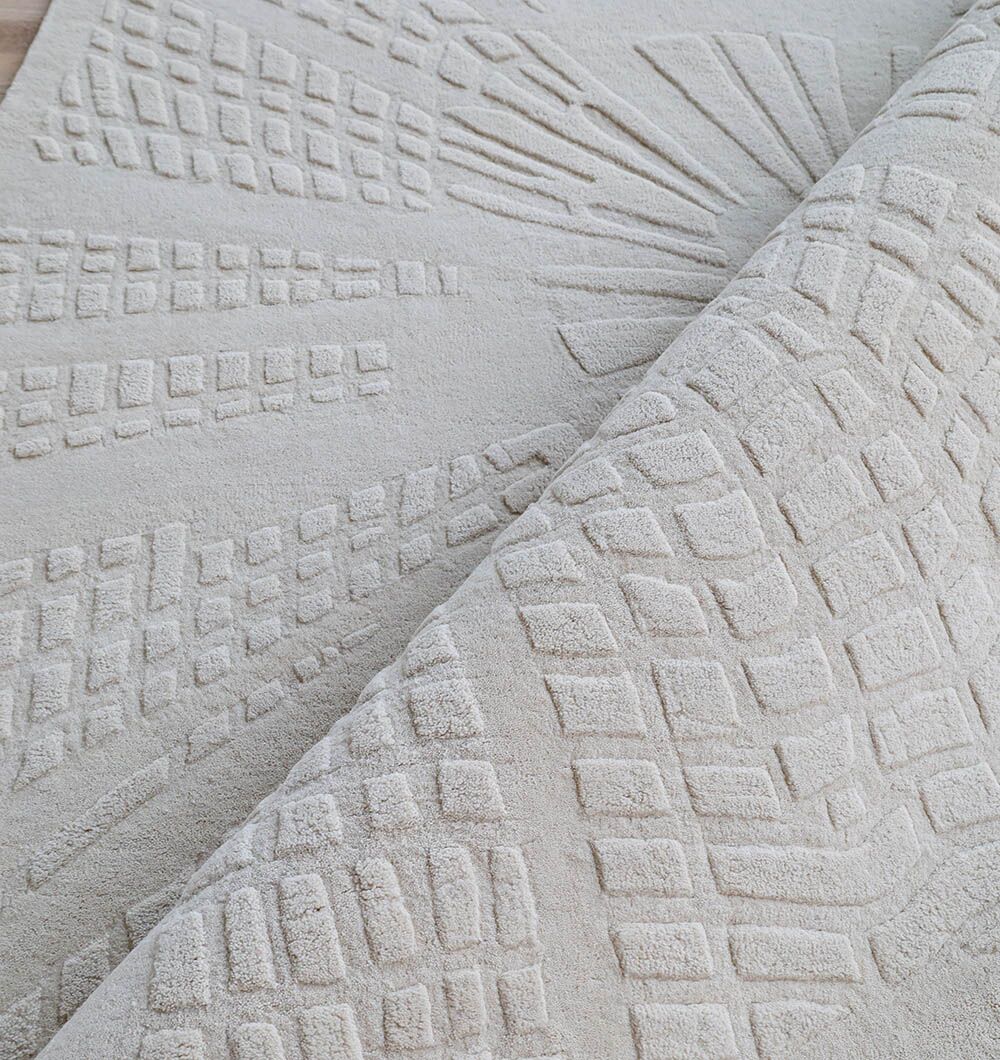 A close-up of the RAMSHA HOME Home Decor Handmade Area Rug - HTW 112 (200x300 cm) in ivory-beige, featuring raised geometric and sunburst patterns, with one corner folded to display both sides of the wool rug.