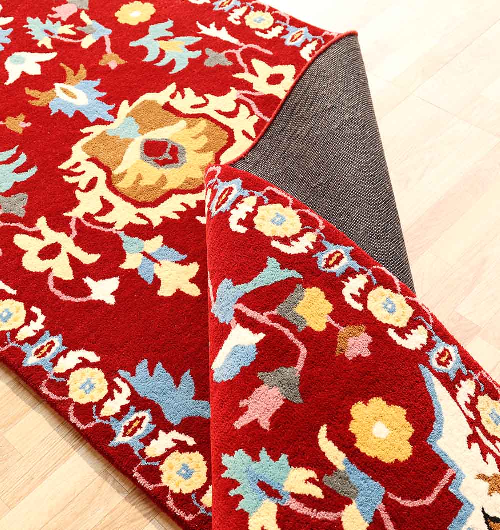 The RAMSHA HOME "Home Decor Handmade Carpet – HTW-118" in red with floral patterns is partially lifted at the corner, showing a non-slip rug pad beneath on a light wood floor.