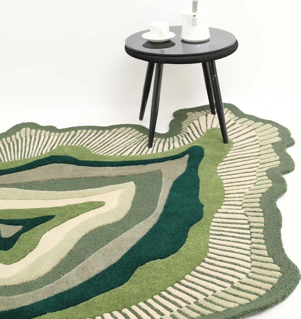 A round side table with black legs holds white cups and a teapot. In front, RAMSHA HOME's Handmade Organic Green Shaped Rug - HTW 123 (200cm) adds layered patterns in green, beige, and gray to the floor.
