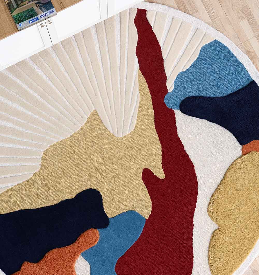 A close-up of the RAMSHA HOME Handmade Wool & Cotton Abstract Round Area Rug HTW 125 (200cm), featuring colorful irregular shapes in red, yellow, blue, navy, orange, and cream on a wooden floor by white cabinets.