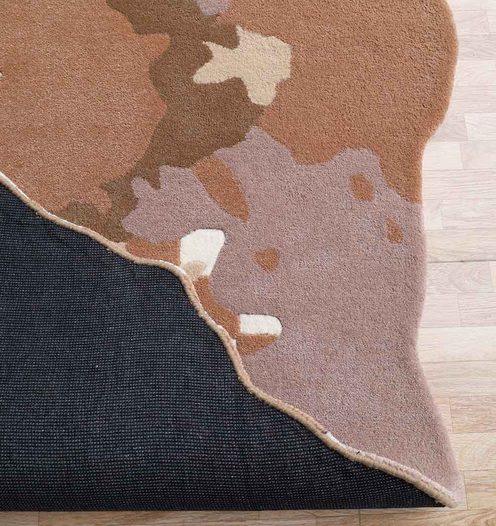 A close-up of the RAMSHA HOME Handmade Multicolor Area Bespoke Rug HTW 128 (200cm) in brown and cream, layered over a black mat on light wood flooring, showcases its unique hand-tufted design.