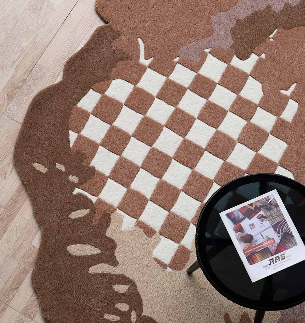 A RAMSHA HOME Handmade Multicolor Area Bespoke Rug HTW 128 (200cm) with a central checkerboard design in brown and beige lies on a light wood floor, partially under a round black glass table with a magazine.