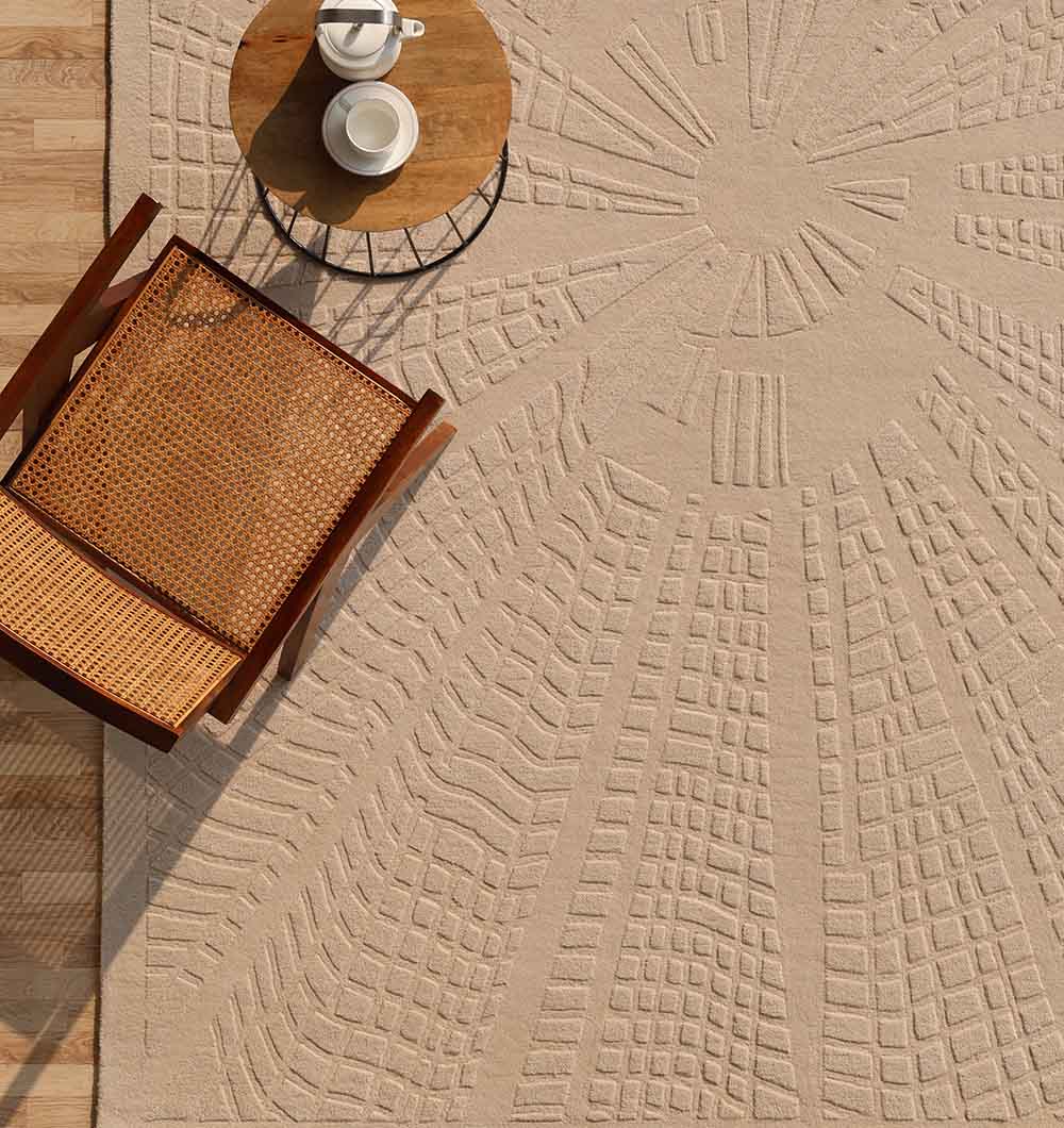 A woven chair and small round table with a teapot and cup sit on the RAMSHA HOME Rectangle Shape Beige Color Handmade Area Rug – HTW 132 (200x300 cm). The rug is set on a wooden floor.