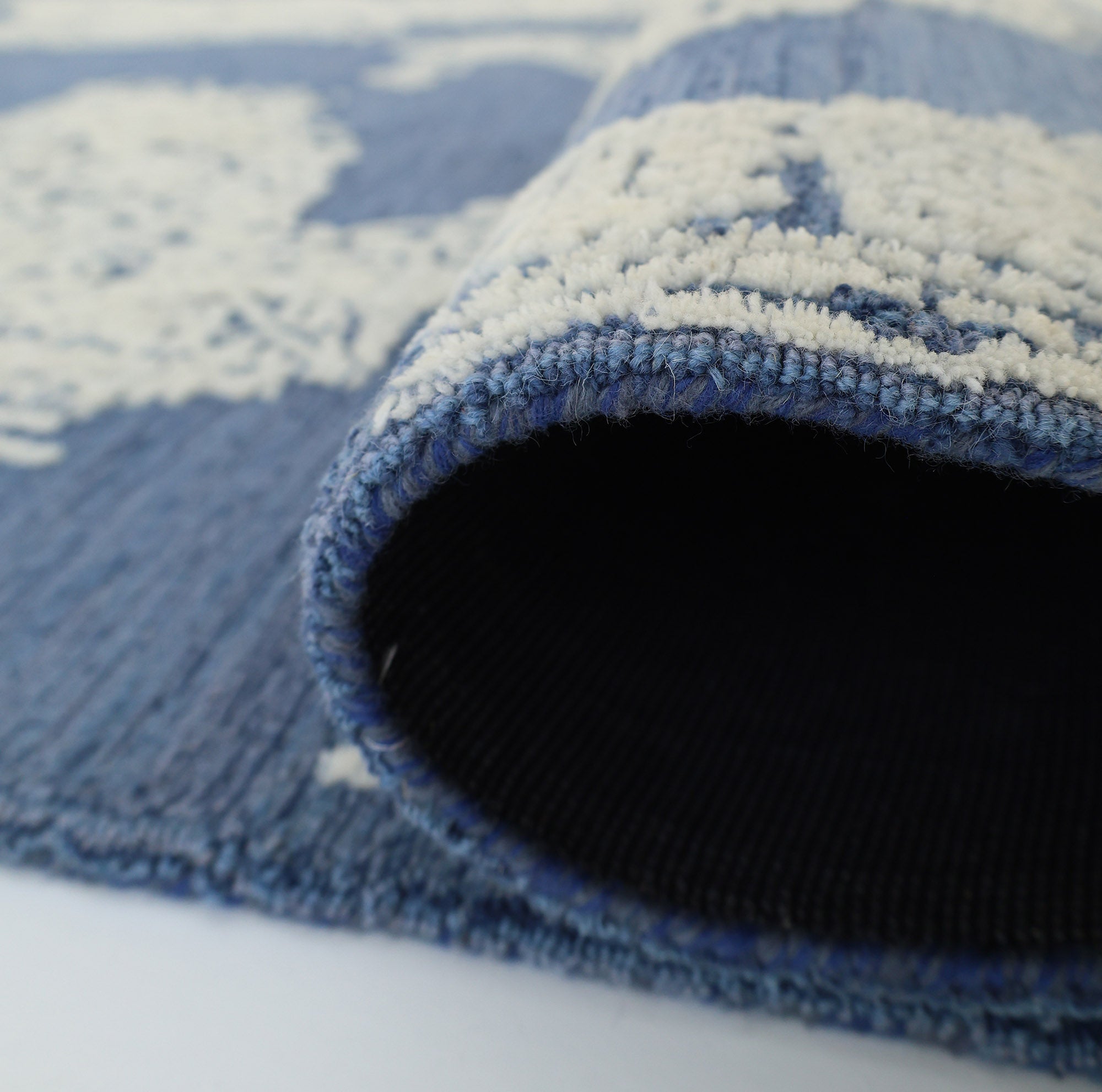 Close-up of the Blue Mosaic Handcrafted Luxury Area Rug- HTW 45 by RAMSHA HOME, with a rolled corner revealing its texture and underside. The out-of-focus background highlights the artisanal detail of this premium rug.