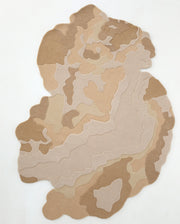 The RAMSHA HOME Contemporary Flow Area Handmade Rug HTWV-153 features an irregular shape with layered abstract beige, tan, and brown patterns, plus a topographic-inspired border on a white background.