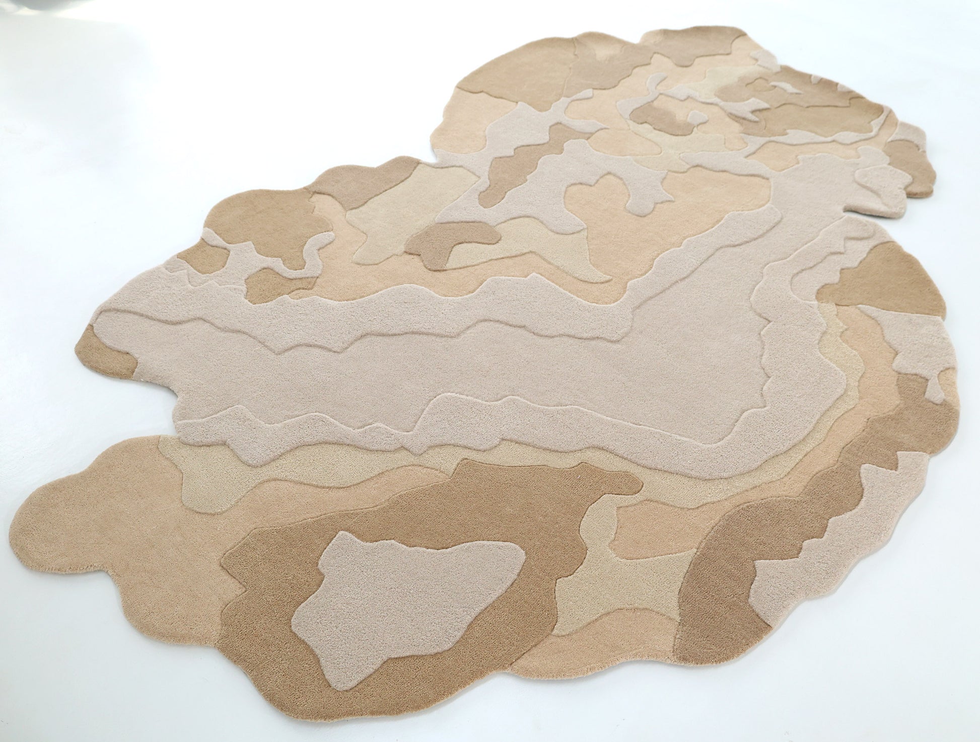 The Contemporary Flow Area Handmade Rug HTWV-153 by RAMSHA HOME features layered organic patterns in beige and tan, resembling a topographic map with an abstract border, shown on a white floor.
