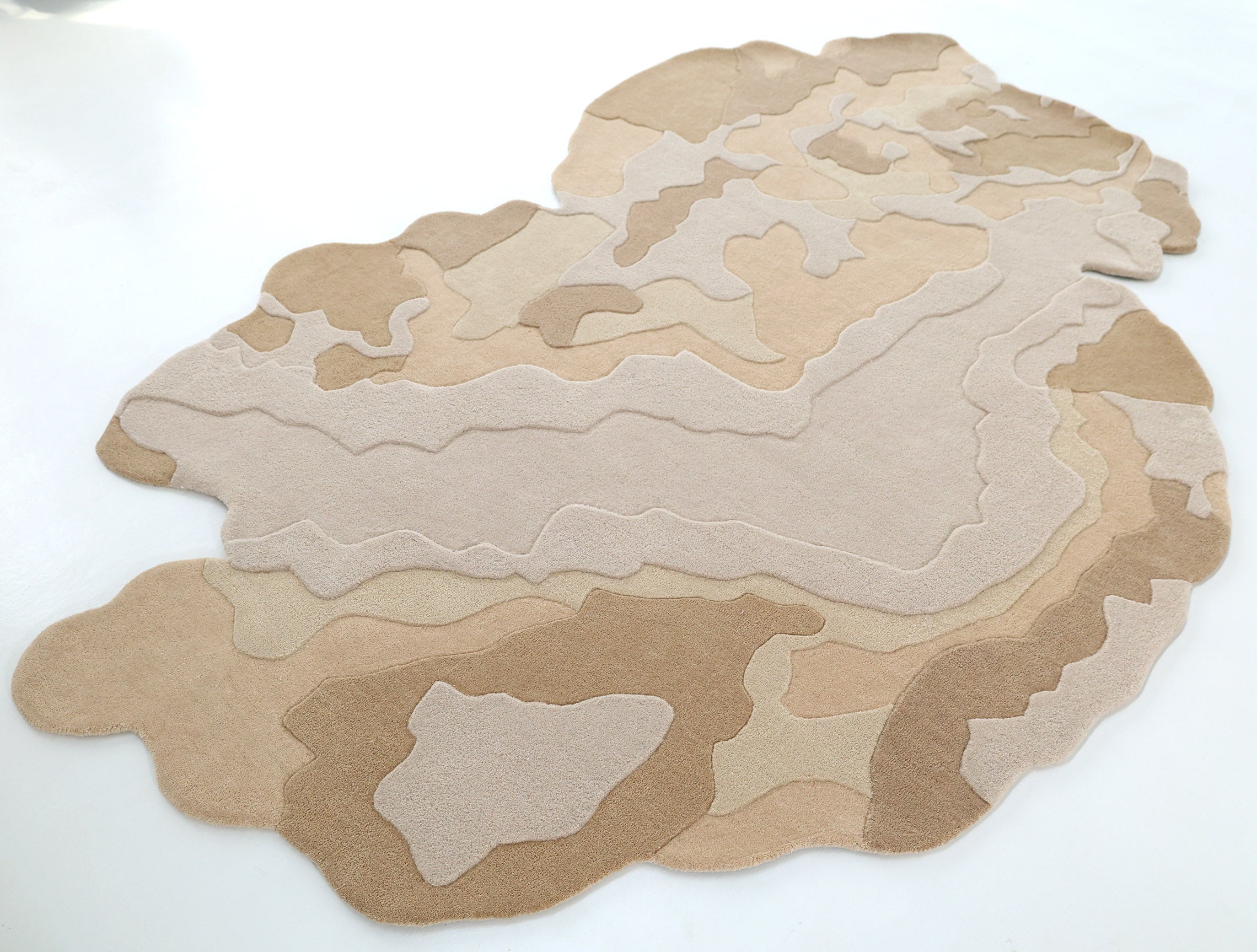 The Contemporary Flow Area Handmade Rug HTWV-153 by RAMSHA HOME features layered organic patterns in beige and tan, resembling a topographic map with an abstract border, shown on a white floor.