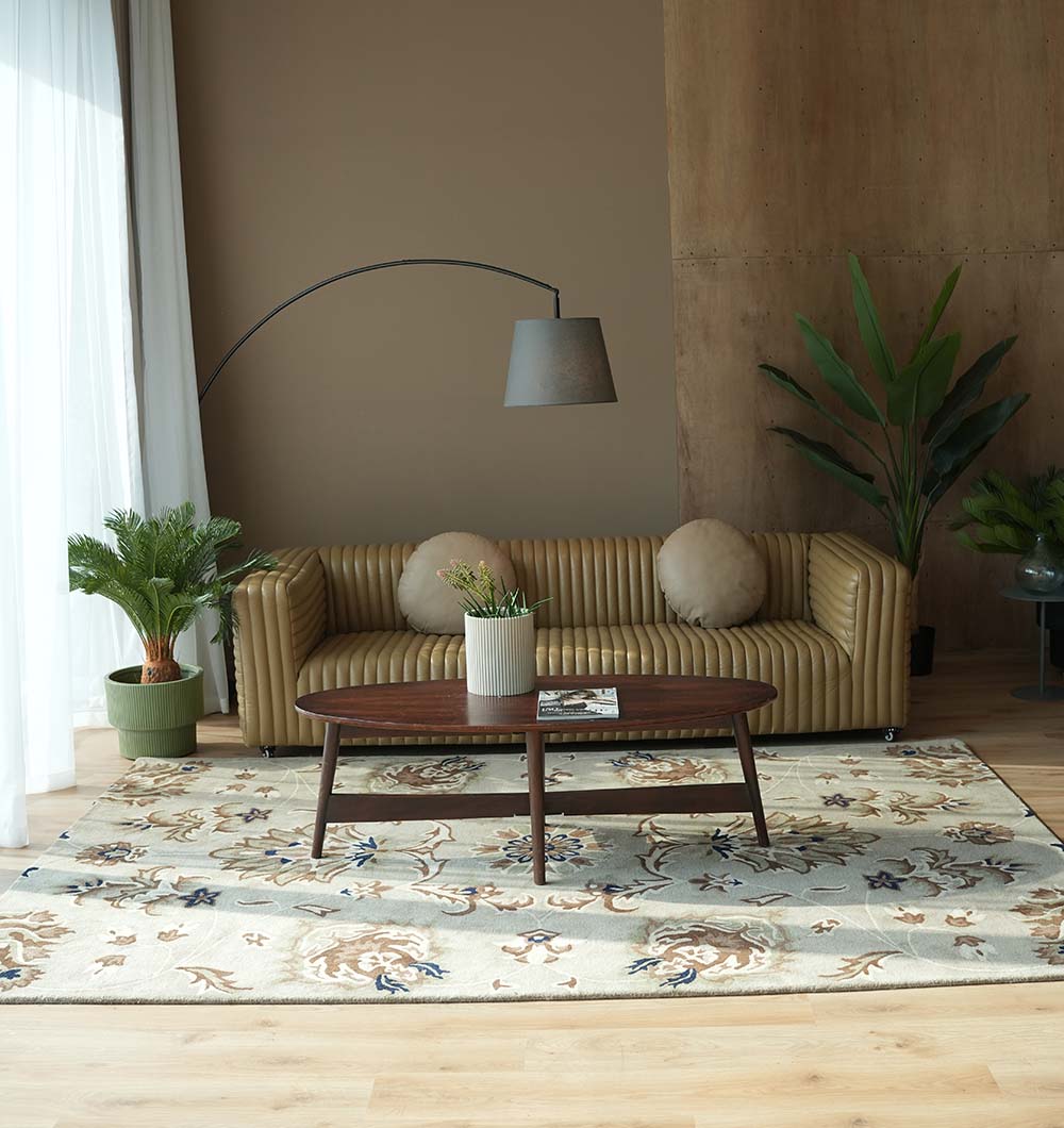 A modern living room features a tan striped sofa, round cushions, plants, a wooden coffee table with a magazine and plant, and an arc floor lamp atop the RAMSHA HOME Handmade Carpet HTW-14 | Classic Persian Elegance.