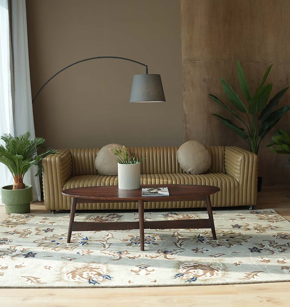 A modern living room with a tan ribbed sofa, round beige cushions, an arc floor lamp, potted plants, a wooden coffee table, and the RAMSHA HOME Handmade Carpet HTW-14 | Classic Persian Elegance by RAMSHA HOME on a wooden floor.