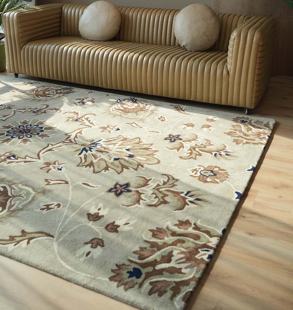 A beige sofa with ribbed upholstery and round cushions sits behind the RAMSHA HOME Handmade Carpet HTW-14, a classic Persian rug in brown, blue, and cream on light wood flooring. Sunlight from the left highlights this elegant living room.