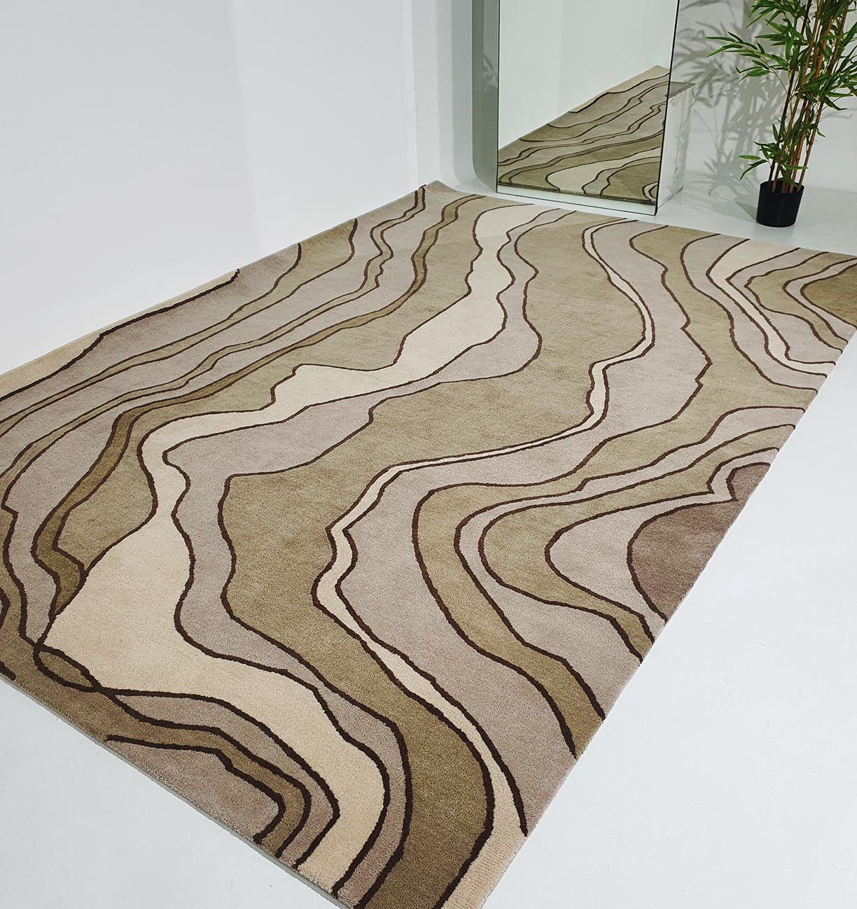 The RAMSHA HOME Beautiful Home Decor Handmade Carpet – HTW-66, featuring curved beige, brown, and tan lines, enhances any space with modern texture and style. Shown here on a white floor near a wall mirror and potted plant.