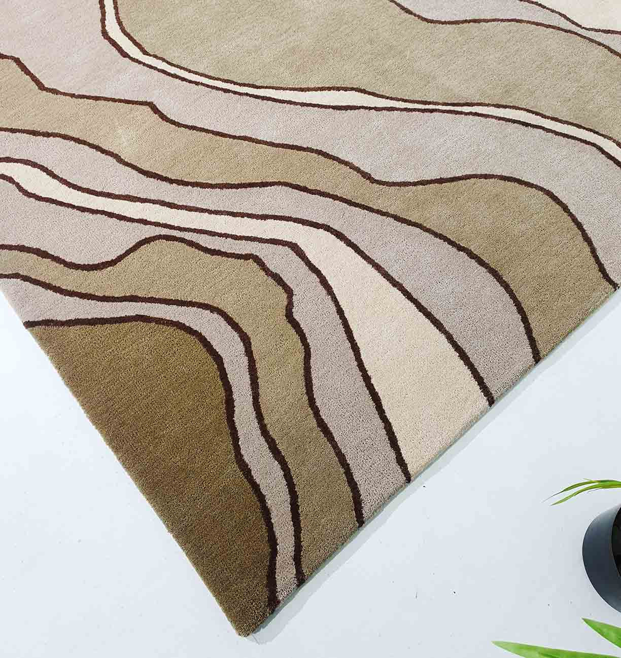 The RAMSHA HOME Beautiful Home Decor Handmade Carpet – HTW-66 is a beige and light brown hand-tufted pure wool rug with wavy dark brown abstract lines, seen on a light floor with a green plant partially visible in the bottom right.