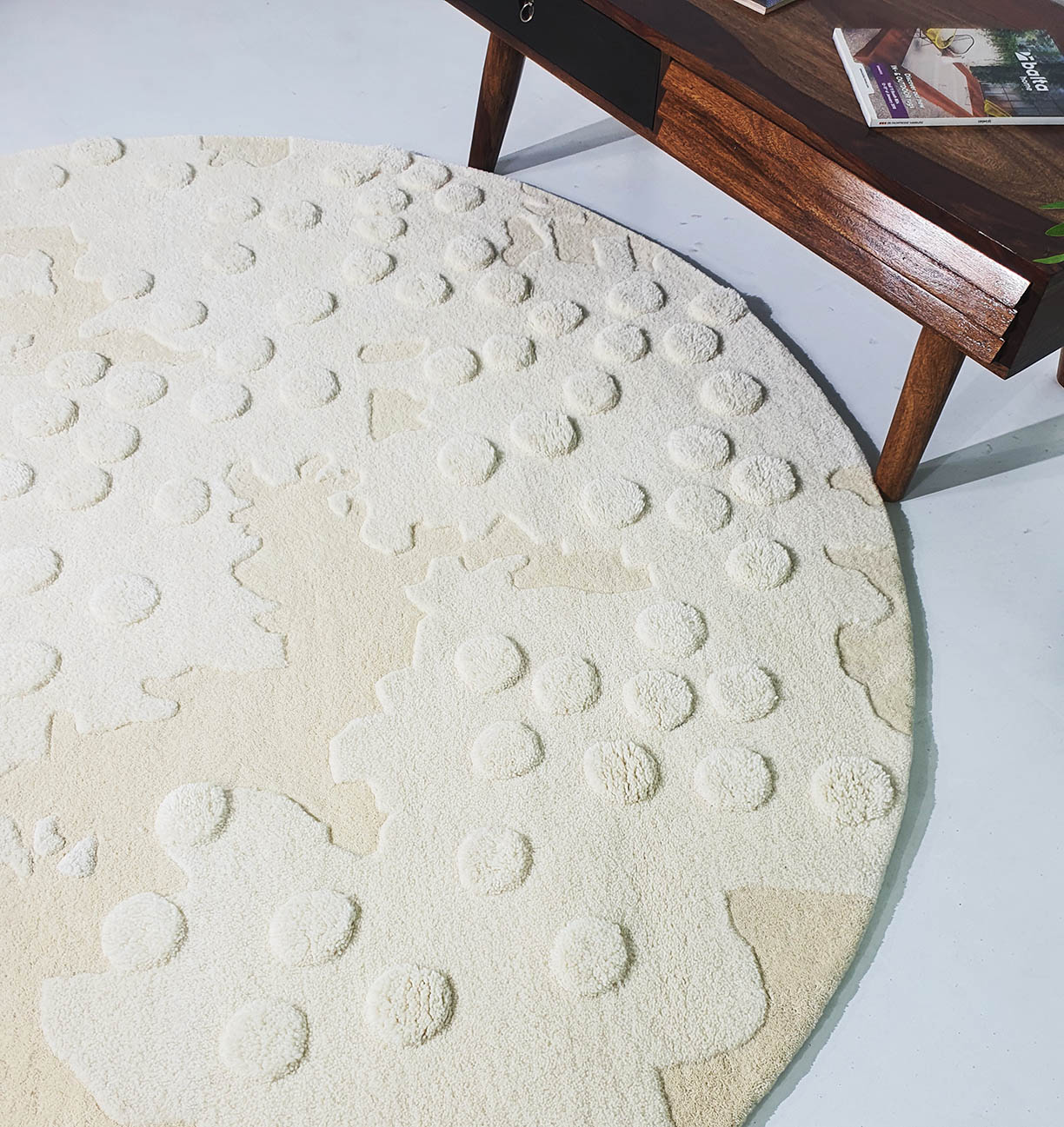 The RAMSHA HOME Round Home Decor Handmade Carpet – HTW-67, a cream and beige hand-tufted wool rug with raised circular patterns, rests on a light floor beside a wooden coffee table with magazines.