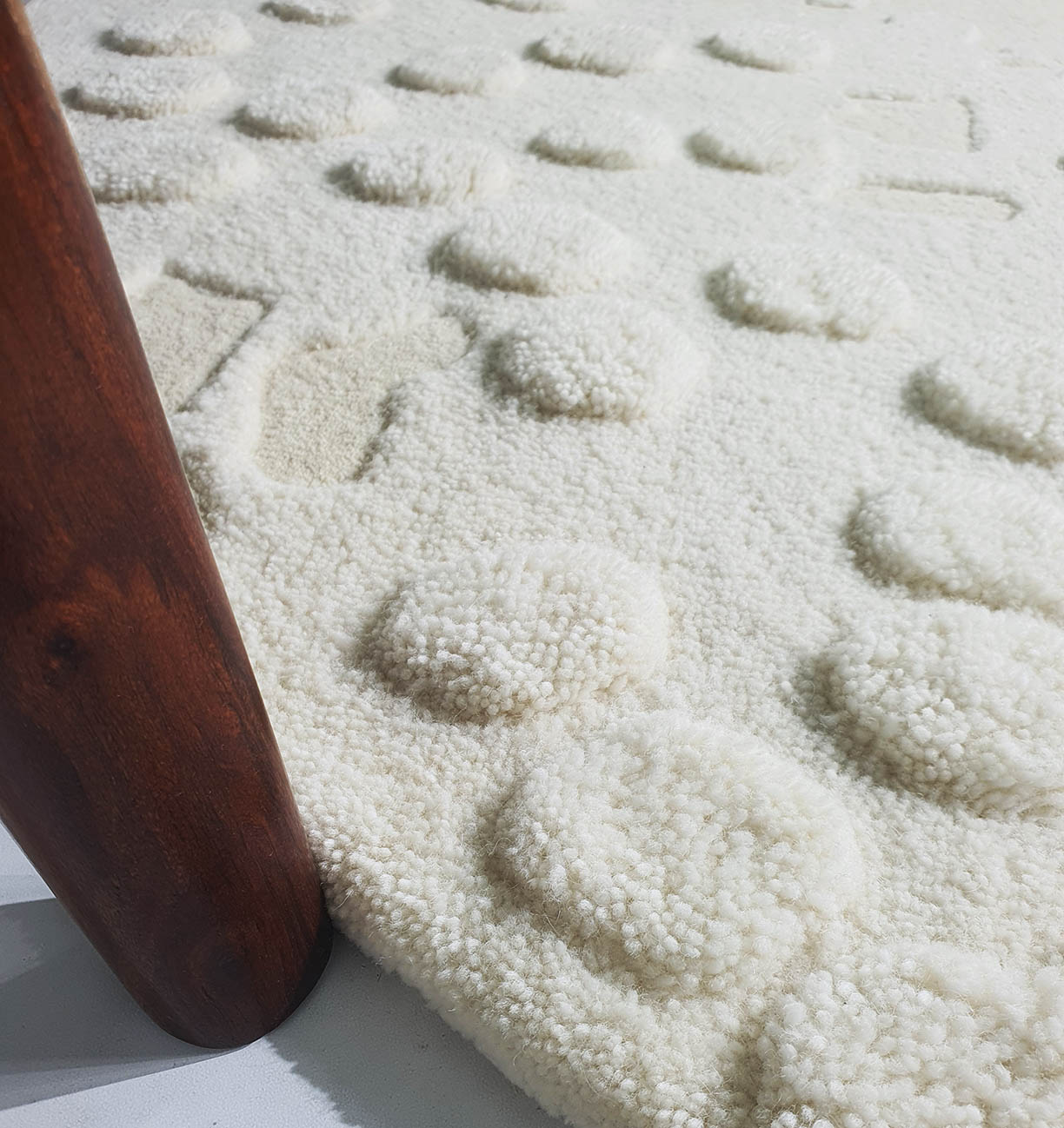 Close-up of the RAMSHA HOME Round Home Decor Handmade Carpet – HTW-67, featuring hand-tufted wool with soft, raised round tufts and a wooden furniture leg resting on it, casting a subtle shadow.