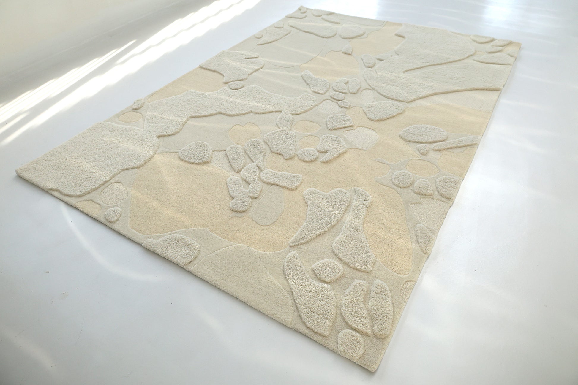 The Creative Multi Color Wool & Cotton Handmade Rug - HTW 69 (200x300cm) by RAMSHA HOME rests on a light floor, sunlight highlighting its raised abstract texture and casting gentle shadows across its neutral-toned design.
