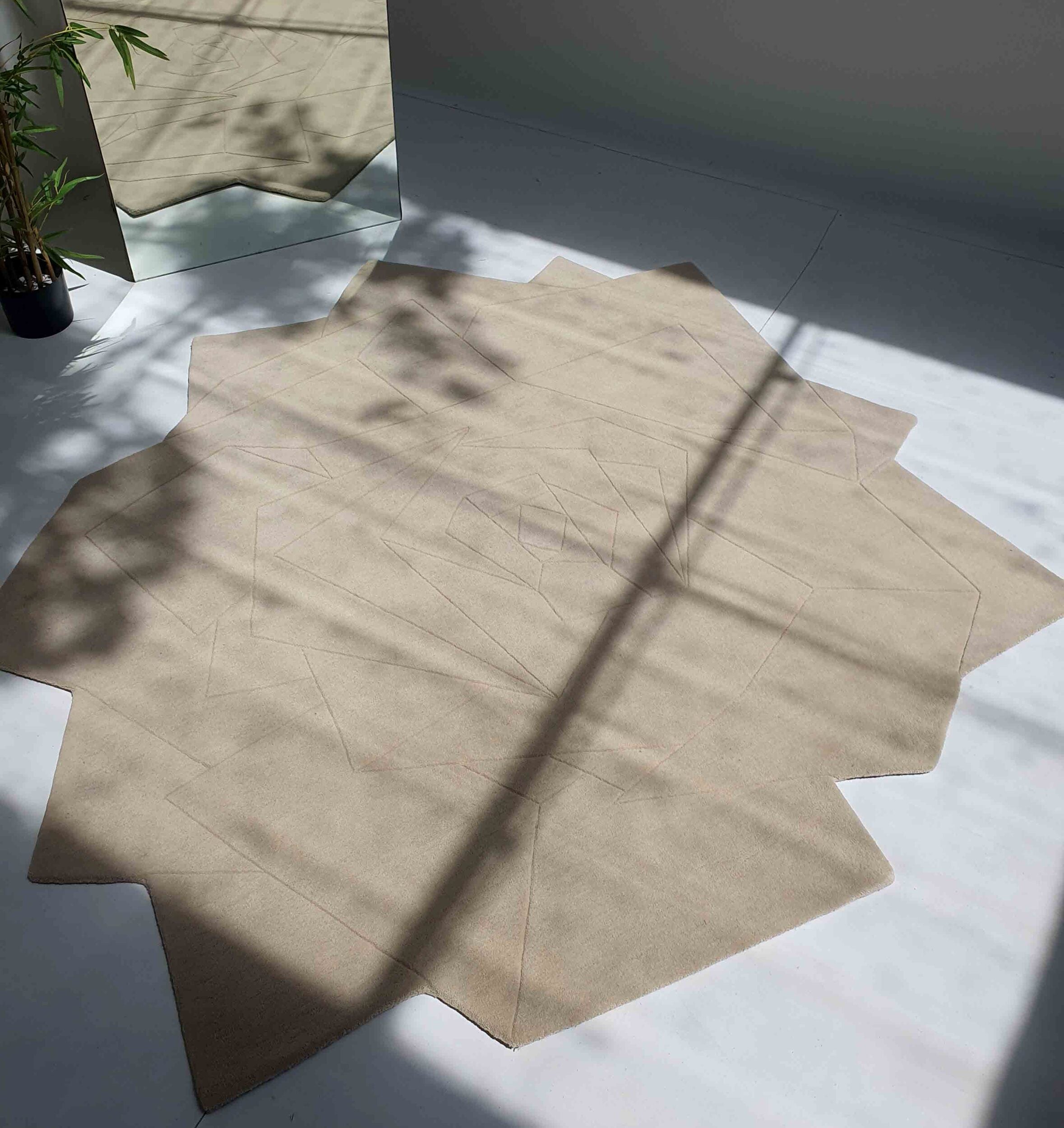 The Stunning Off Flower Shape Handmade Rug - HTW 77 (200 cm) by RAMSHA HOME lies on a light floor with windowpane and plant shadows; a potted bamboo and mirror are in the background.