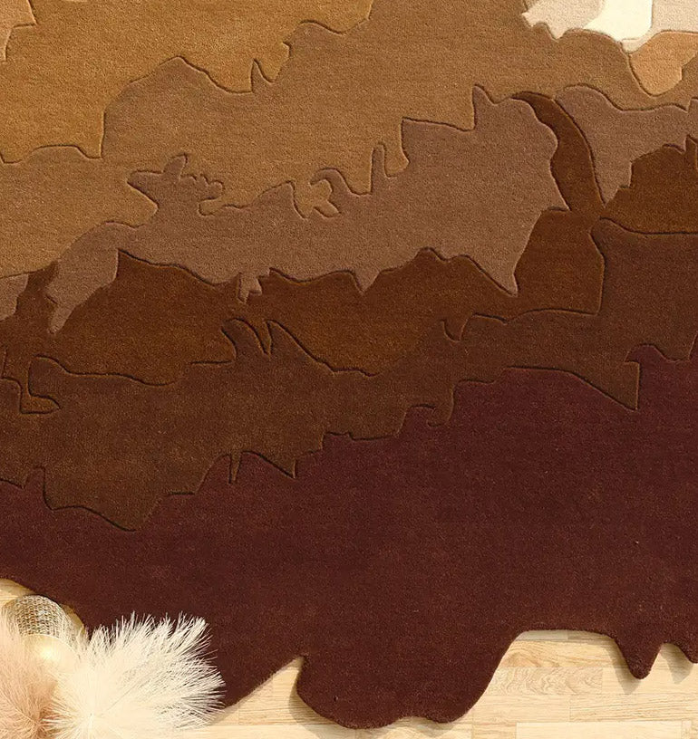 The RAMSHA HOME Handmade Shape Brown Color Area Rug - HTW 86 features abstract, wavy brown, tan, and beige layers with an irregular edge and soft beige accents in the bottom left corner, resembling a topographical map.