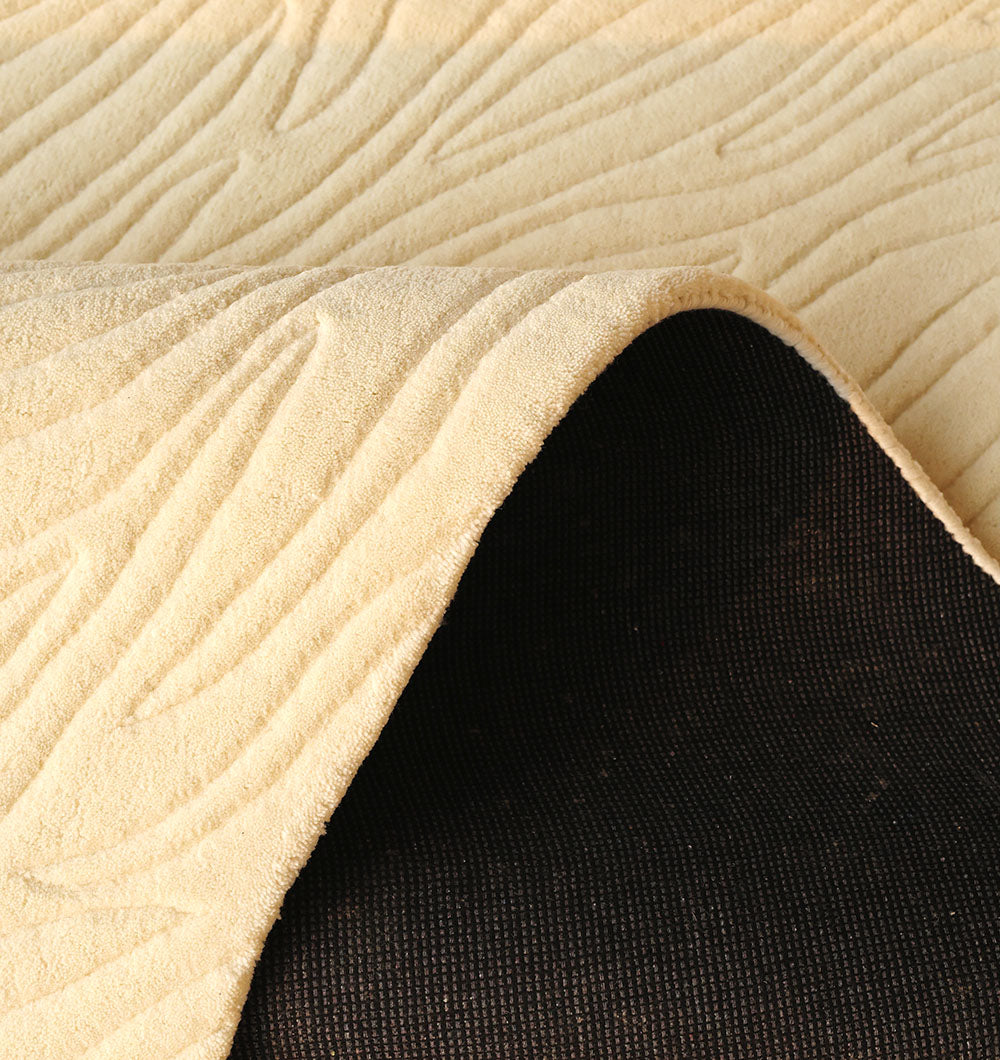 A close-up of the RAMSHA HOME Natural White Color Area Carpet - HTW 88 shows its textured beige wavy patterns, with part of the rug lifted to reveal a dark, non-slip backing underneath.