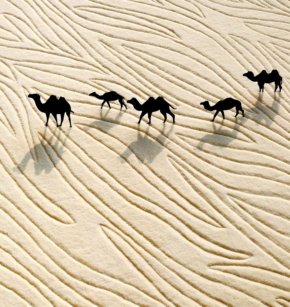 Five camels walk in a line on sand with wavy patterns, casting long shadows—evoking the design of the RAMSHA HOME Natural White Color Handmade Area Rug - HTW-89 (300x400 cm).