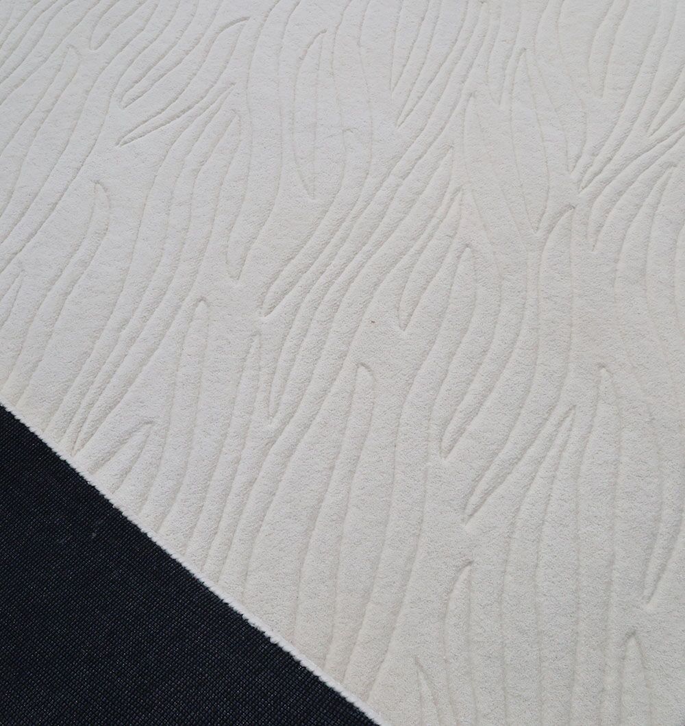A close-up of the RAMSHA HOME Off White Color Decor Area Rug - HTW-94 (200X300 CM) shows its textured hand tufted wool with a raised abstract wavy pattern, bordered by a solid black fabric strip in the bottom left corner.