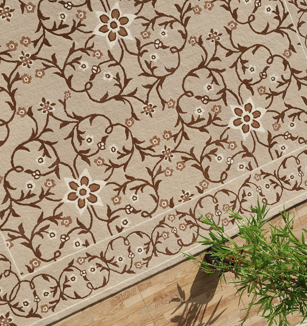 The RAMSHA HOME Exquisite Multi Color Decor Handmade Rug - HTW 99 (300x400 CM) in beige with an intricate brown floral and vine design lies on a wooden floor, with part of a green plant visible in the lower right corner.