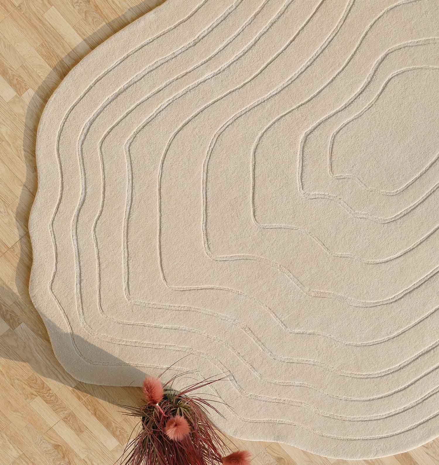 The RAMSHA HOME Hand Tufted Beige Color Decor Rug HTWV-108, featuring modern concentric patterns, rests on a light wood floor; a vase with pink dried flowers brings charm to the top right corner.