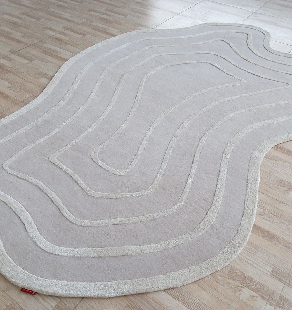 The Beautiful Off White Handmade Rug - HTWV-112 (200x300cm) by RAMSHA HOME, featuring hand tufted concentric lines and wavy edges, adds an abstract touch to the light wood floor.