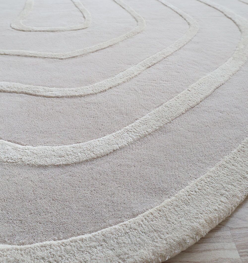 A close-up of the RAMSHA HOME Beautiful Off White Handmade Rug - HTWV-112 (200x300cm) shows its hand-tufted, abstract curved lines on a light wooden floor.