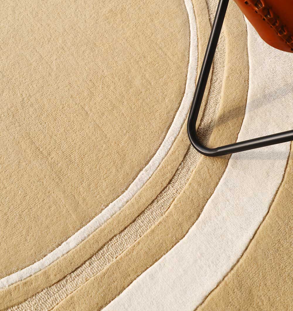 Close-up of the RAMSHA HOME Multi Color Handmade Rug - HTWV-120, featuring beige and cream curved patterns. The metal leg of a chair with a brown leather seat appears in the top right corner.