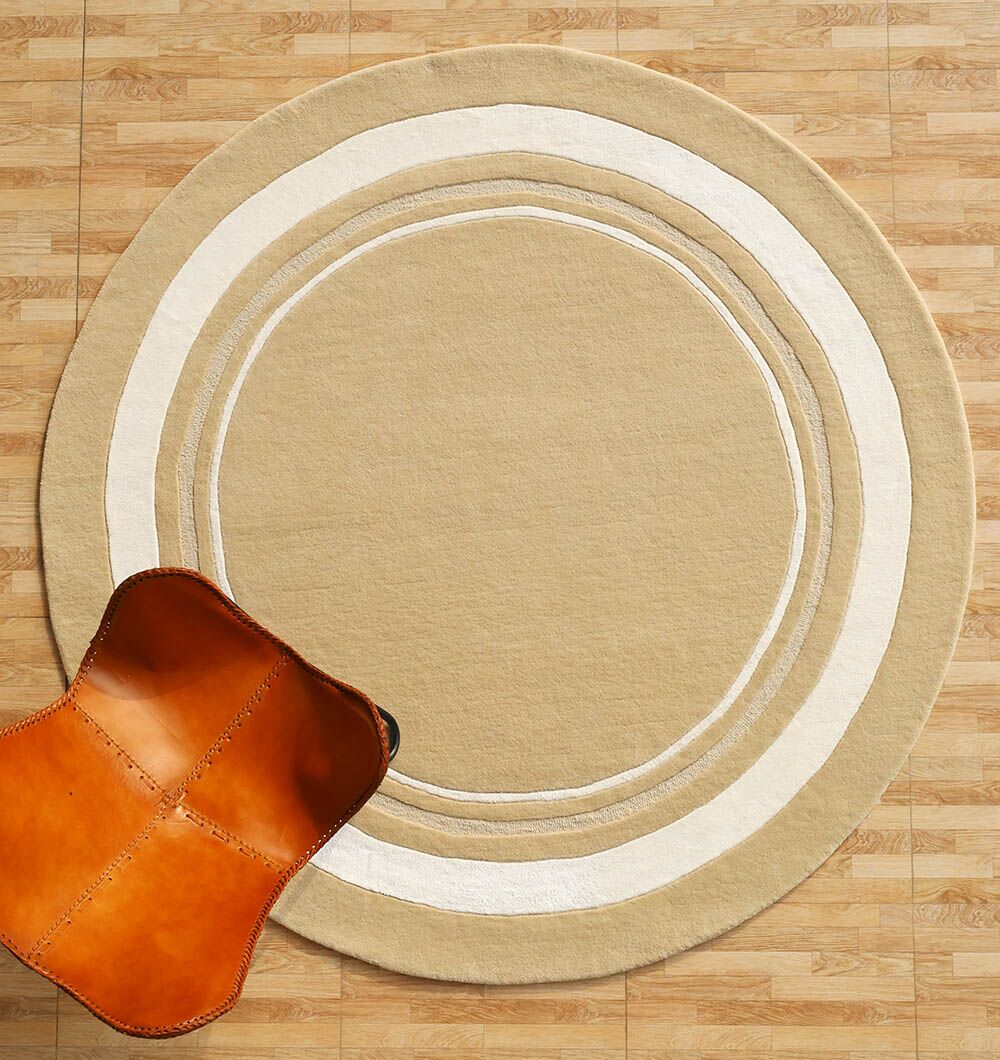The RAMSHA HOME Multi Color Handmade Rug - HTWV-120, with beige and white concentric rings, is displayed on a light wood floor. A tan leather chair with visible stitching appears in the lower left corner.