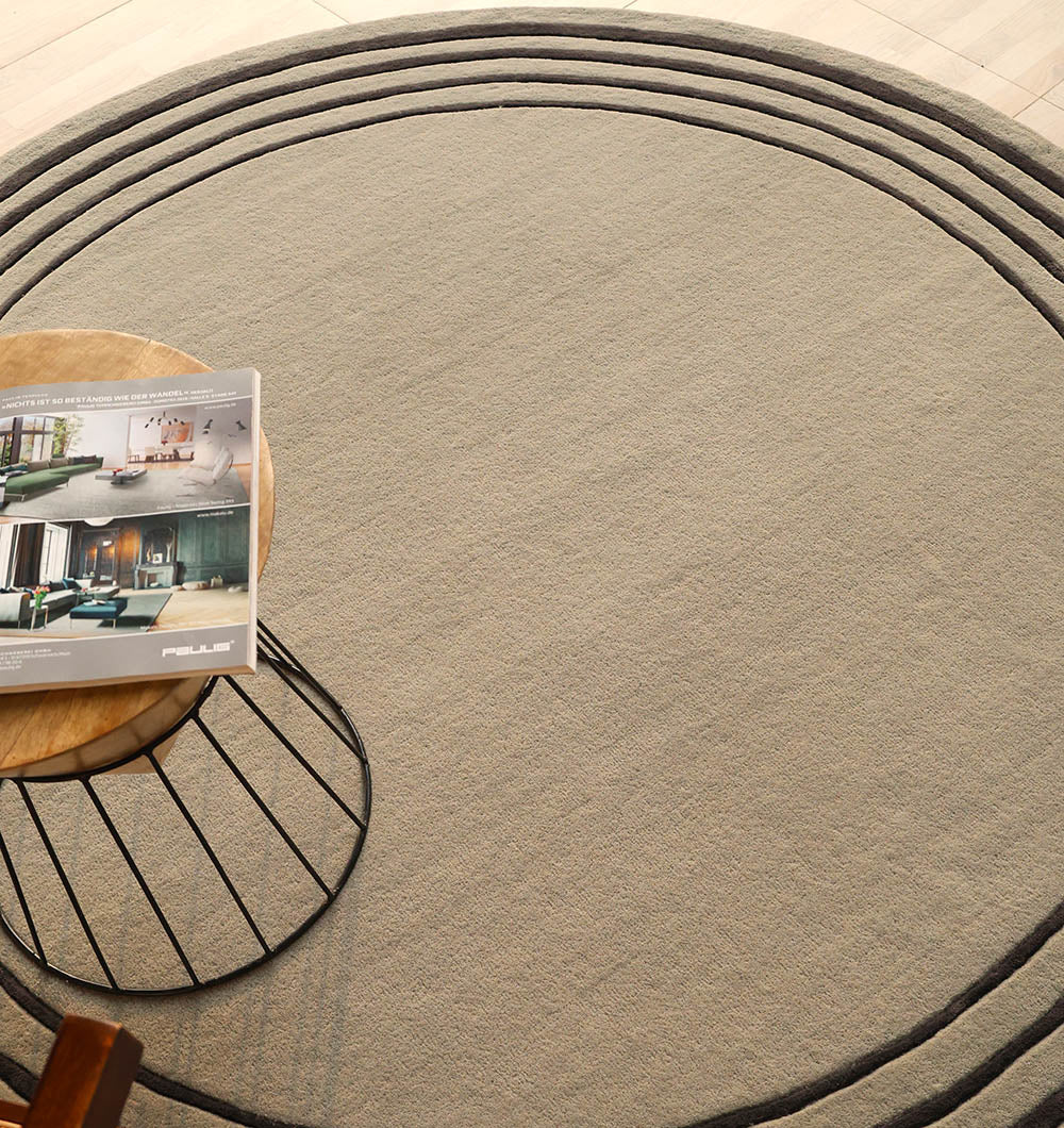 Handmade round rug placed under a table in a living space, adding sophisticated black and grey tones to the area.