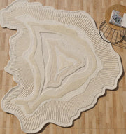 The RAMSHA HOME Natural Handmade Area Rug (HTWV-126), a cream and beige wool blend with wavy edges and concentric patterns, lies on a light wood floor by a small round side table holding a magazine and cup.