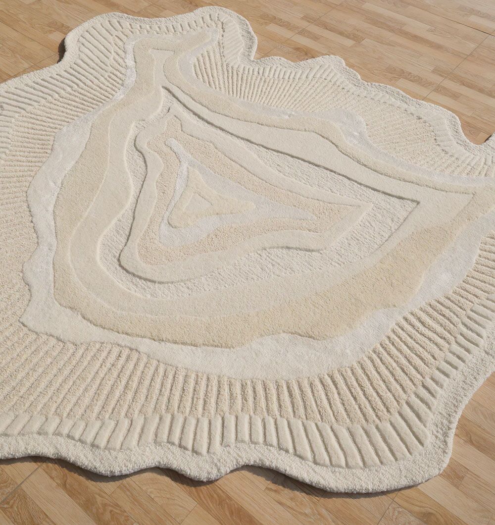 The RAMSHA HOME Natural Handmade Area Rug - HTWV-126, a beige wool blend with textured, topographic-inspired patterns and an irregular shape, is displayed on a light wooden floor.