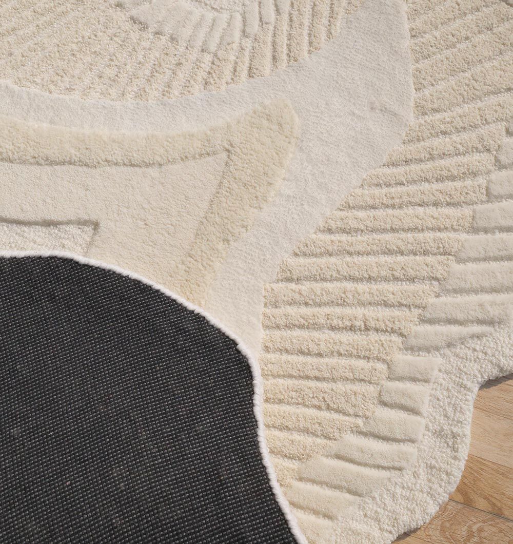 Close-up of the RAMSHA HOME Natural Handmade Area Rug - HTWV-126, featuring cream and beige curved patterns with a black section, edge resting on a wooden floor.