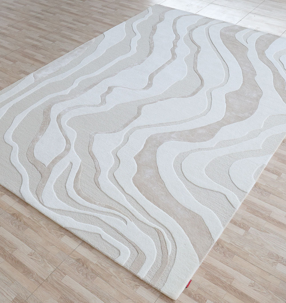 The RAMSHA HOME Handcrafted Living Room Area Rug – HTWV-127, featuring cream and beige wavy patterns, is displayed on a light wood floor in a bright, spacious room.