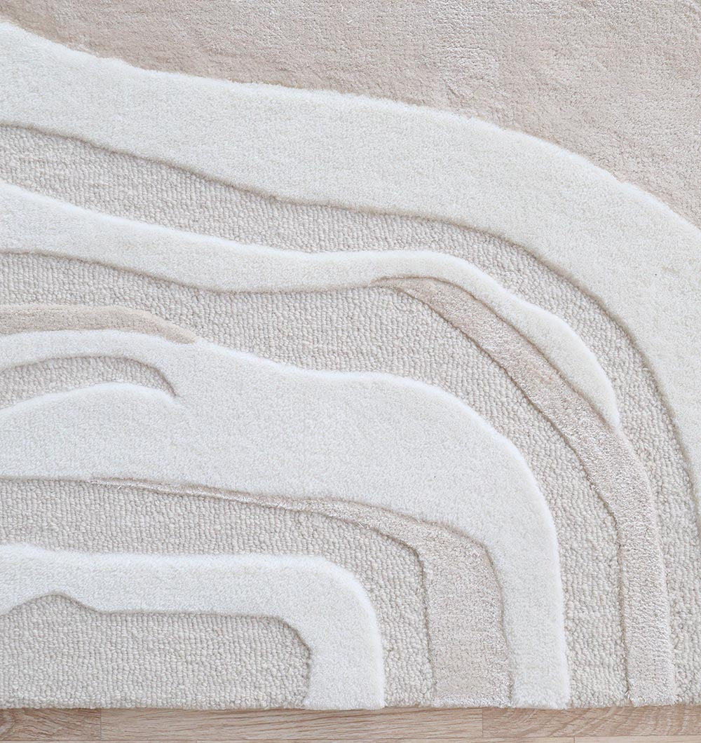 The RAMSHA HOME Handcrafted Living Room Area Rug – HTWV-127 features a modern abstract cream and beige design with layered, curved lines like waves or geological patterns, shown on a light wood floor.