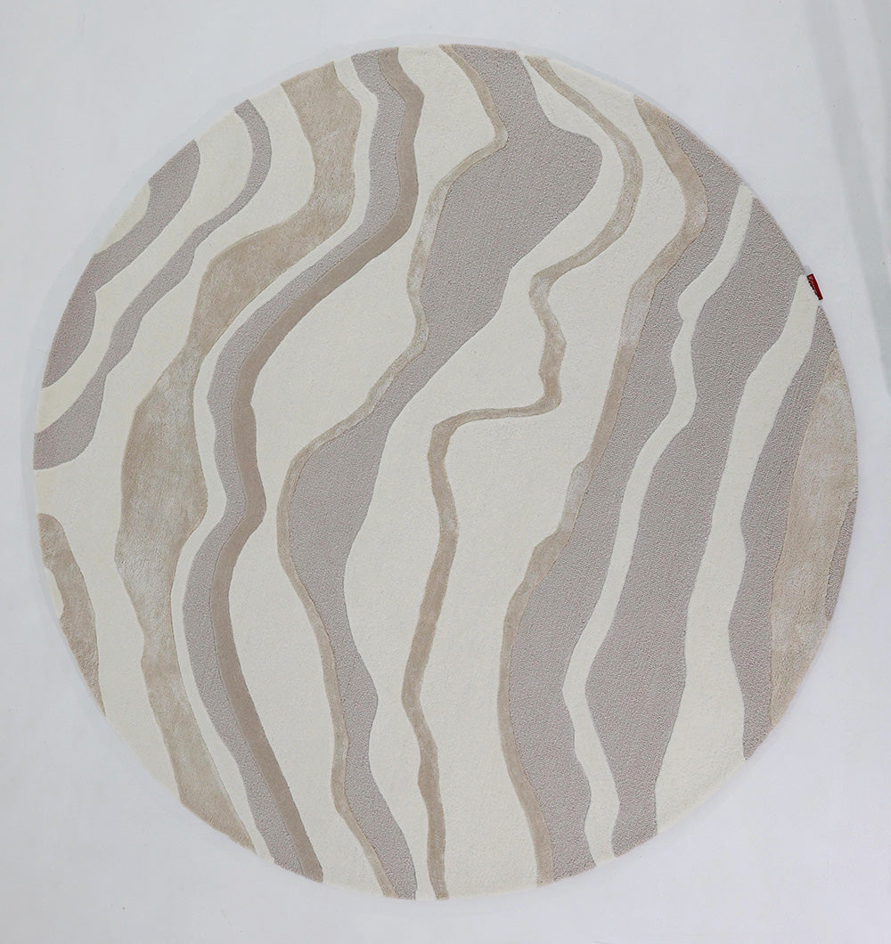 The RAMSHA HOME Handcrafted Living Room Area Rug – HTWV-127 is a round, handtufted rug showcasing an abstract wavy pattern in beige, taupe, and cream on a white background.