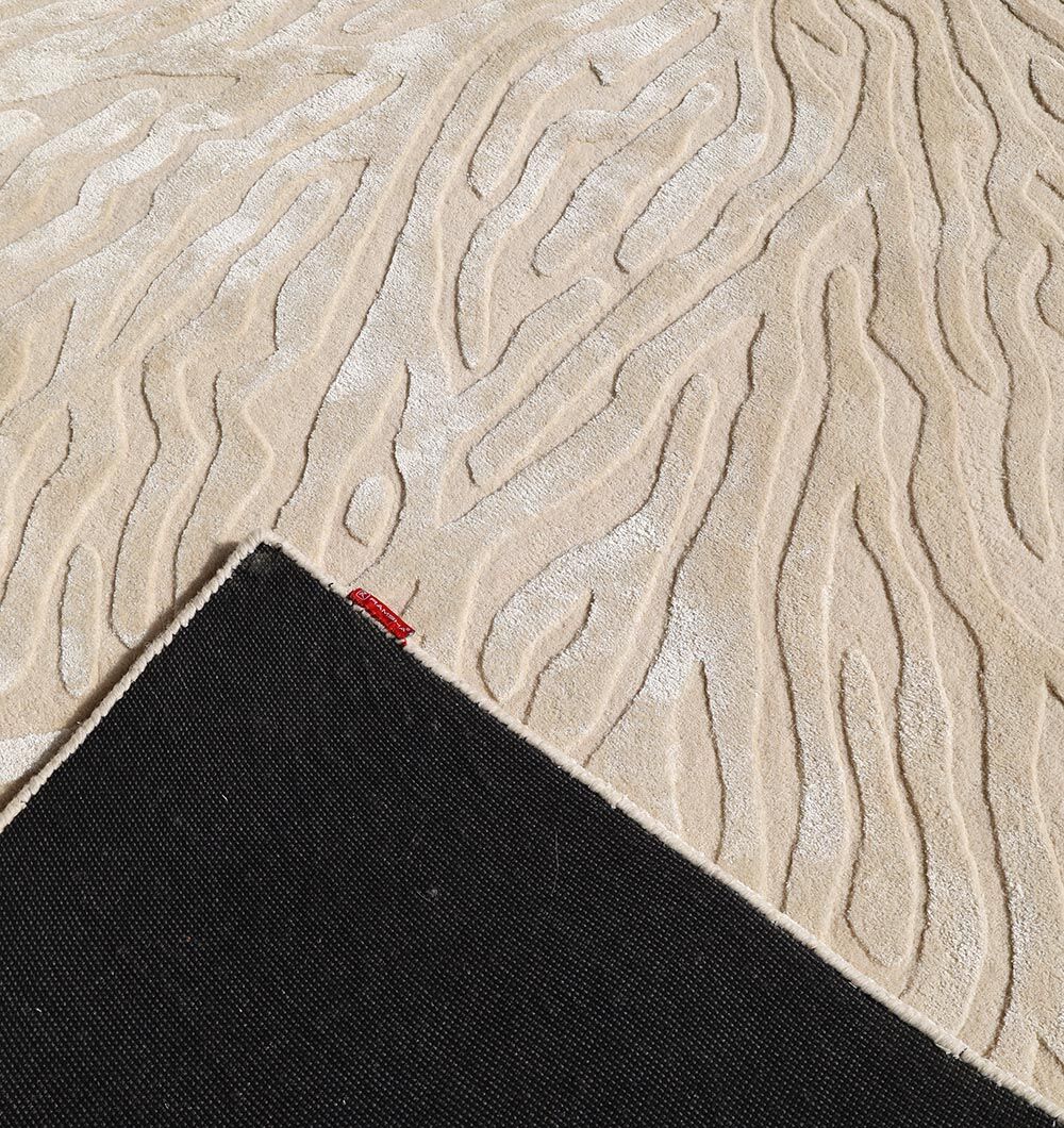 The RAMSHA HOME Natural White Color Handmade Area Rug (HTWV-130) features a raised, wavy abstract pattern, folded to reveal a black non-slip backing and red tag. This hand-tufted rug blends wool and viscose for extra texture and softness.