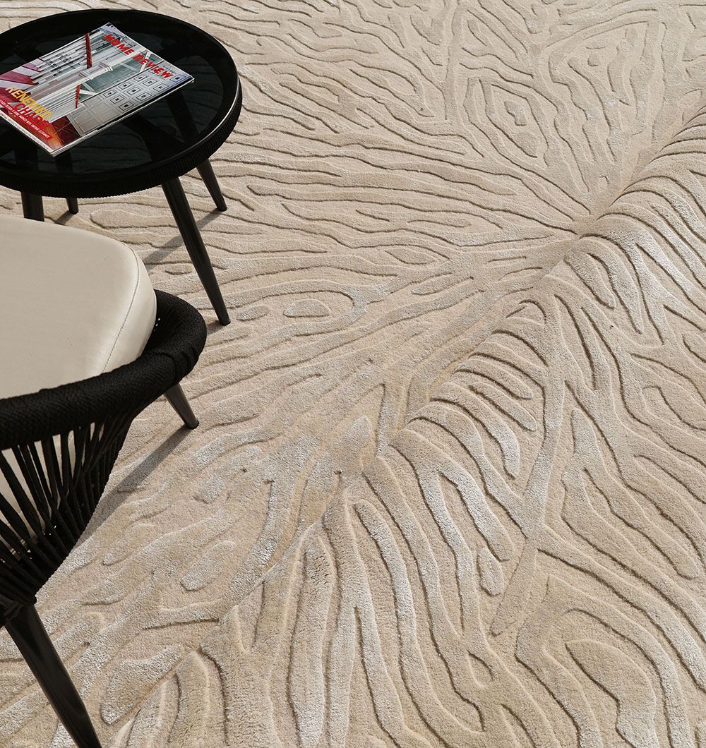 The RAMSHA HOME Natural White Color Handmade Area Rug - HTWV-130, featuring abstract wavy patterns, is partially rolled up next to a black round side table topped with magazines and a light-colored cushion.