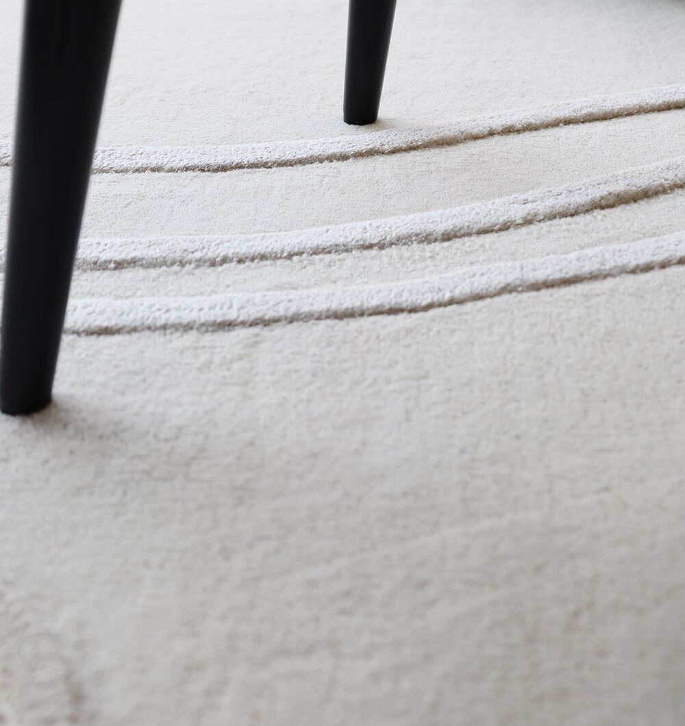 Close-up of the RAMSHA HOME Multi Color Handmade Area Rug - HTWV-133 featuring textured beige hand-tufted wool with raised curved lines; two black angled furniture legs are partially visible at the top of the image.