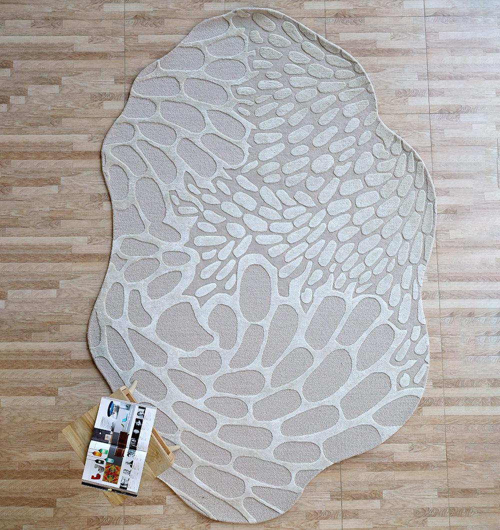 The Organic Flow Hand-Tufted Rug – Soothing Beige Textured Elegance HTWV-134 by RAMSHA HOME, with an irregular pebble-like pattern in beige and cream, lies on a light wood floor. A wooden tray with a magazine and drinks sits at the rug's bottom left corner.