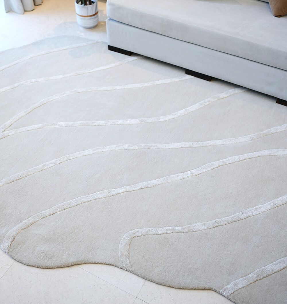 A RAMSHA HOME Multi Color Handmade Area Rug - HTWV-136 (200x300 cm) with wavy patterns is placed on the floor beside a light gray sectional sofa. A small potted plant stands in the corner behind the sofa.
