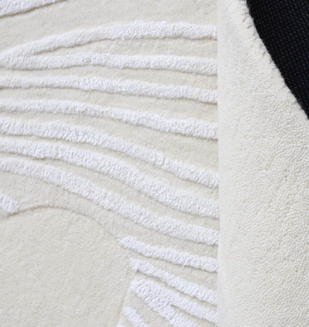 Close-up of the Off White Color Handmade Area Rug (HTWV-140, 200x300 cm) by RAMSHA HOME, featuring modern raised wavy textures in cream and a folded corner showing the black non-slip backing.